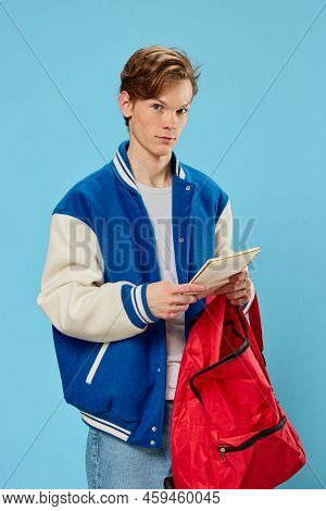 A Pensive Student In A Blue Stylish Bomber Jacket Stands With A Notebook In His Hands And Looks Away