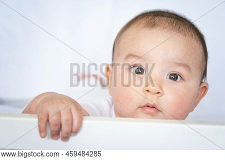 Cute Portrait Of A Baby In A Crib Close-up. A Child In White Clothes On White Underwear. Tenderness 