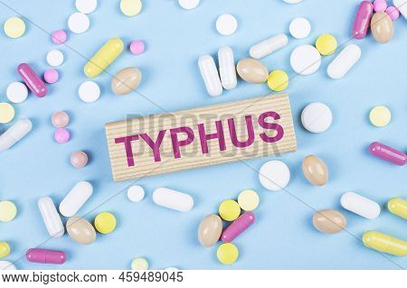 On A Blue Background, Multi-colored Pills And A Wooden Block With The Text Typhus. View From Above. 