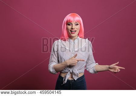Carefree Happy Adult With Pink Hair Pointing Sideways In Studio, Indicating Left Or Right Directions