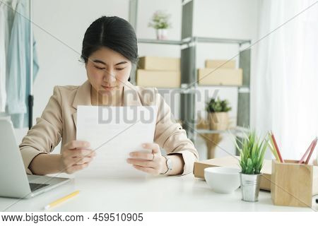 Young Asian Female Freelan Sit Reading Report On Paper In Online Clothing Store..
