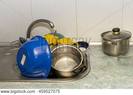 Dirty And Unwashed Dishes Are Stacked In The Kitchen Sink. Unwashed Cups, Plates, Pots, Forks And Sp