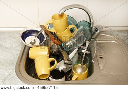 Dirty And Unwashed Dishes Are Stacked In The Kitchen Sink. Unwashed Cups, Plates, Pots, Forks And Sp