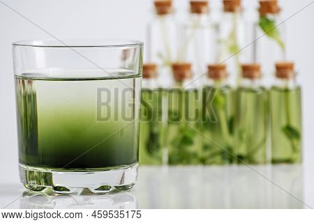 Chlorophyll Extract Is Poured In Pure Water In Glass Against A White Grey Background And Micro Green