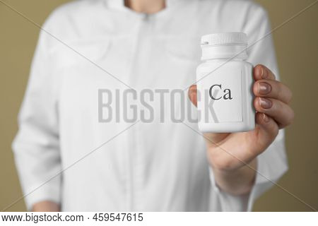Calcium Supplement. Doctor Holding Bottle With Pills On Beige Background, Closeup