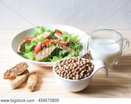 Front View Of Soy Bean Seeds In White Bowl, Tempeh In Salad Dish And Soy Milk On Wooden Table, Produ