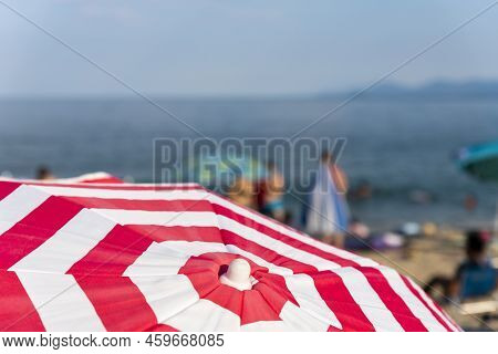 Striped Beach Umbrella At The Beach With Tourists And Sea In Background