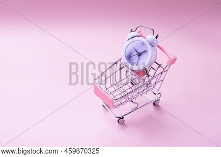 White Alarm Clock And Toy Shopping Cart Isolated On Pink. Watch In The Shopping Cart, Lack Of Time, 