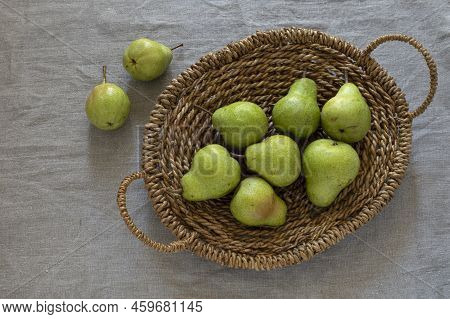 Top View Of Green Barlett Pears In The Brown Woven Backet With Handles On Natural Linen Fabric Backg