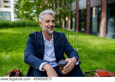 Mature Businessman Resting And Sitting Barefoot In Park With Cup Of Coffee, Feeling Free, Escaping F