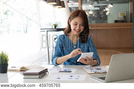 Smiling Pretty Girl Working On Laptop Computer While Sitting At Office Table, Taking Notes In A Diar