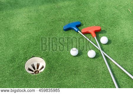 Mini-golf Clubs And Balls Of Different Colors Laid On Artificial Grass