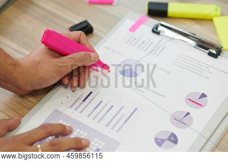 Hands Of Manager Highlighing Important Figures In Report With Bright Pink Color