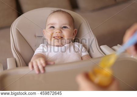 Mother Feeding Porridge To Her Happy Cheerful Baby Boy Using Spoon, Cheerful And Happy Baby Sitting 