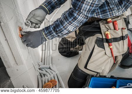 Professional Electrician In Protective Gloves And Tool Belt Working On Installing Power Sockets In T