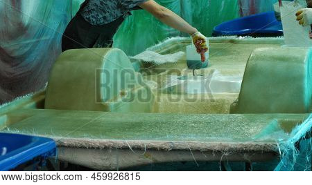 A Man Uses A Paint Roller To Apply Adhesive To Fiberglass, Gluing The Hull Of A Pedal Catamaran. Bui