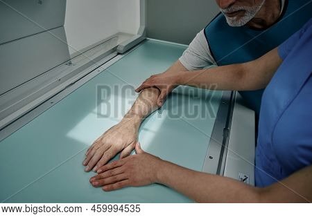 Radiologist Doing X-ray Of Male Patients Hand On Modern X-ray Machine, Placing Hand In Right Place O