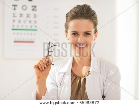 Happy Ophthalmologist Doctor Woman With Eyeglasses In Front Of Snellen Chart