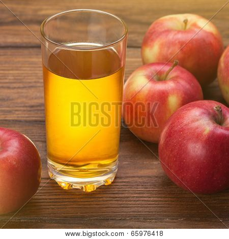 Glass of apple juice and red apples on wooden background