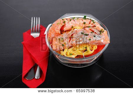 fresh fried natural pink salmon on italian traditional tagliatelle backed with tomato and vegetables served over black wooden table