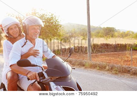 Mature Couple Riding Motor Scooter Along Country Road