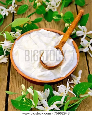 Yogurt in clay bowl with spoon and flowers of honeysuckle