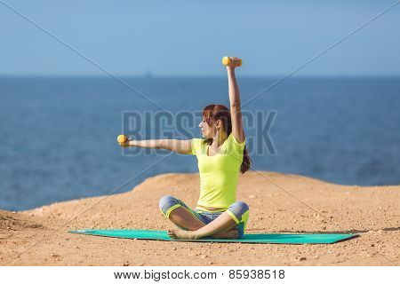 A young woman fitness trainer, shows a set of exercises with dumbbells.