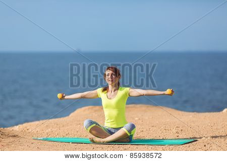 A young woman fitness trainer, shows a set of exercises with dumbbells.