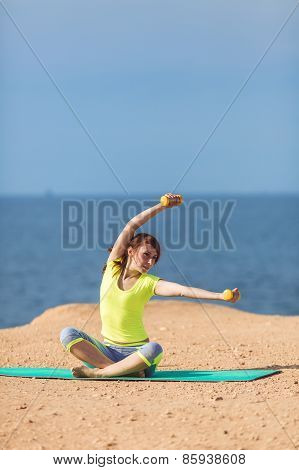 A young woman fitness trainer, shows a set of exercises with dumbbells.
