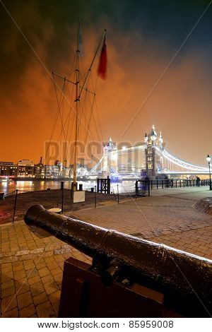 Cannon and Tower Bridge at night at St. Katherine Dock in London.
