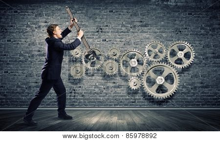 Young businessman fixing gears mechanism with wrench