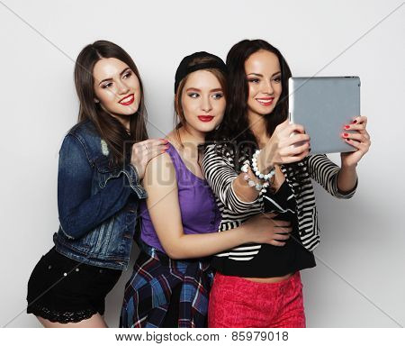 Three girls friends taking selfie with digital tablet, studio shot over gray vackground