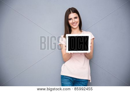 Smiling young woman showing tablet computer screen over gray background