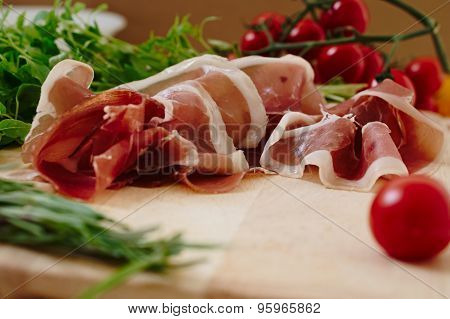 Gourmet prosciutto ham in a rustic setting with cherry tomatos, rosemary and basil