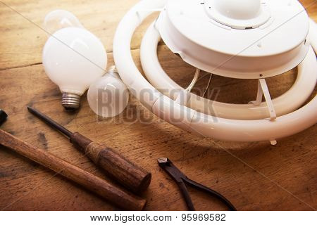 Replacing obsolete or old lighting equipment. Incandescent lamp or light bulbs and flourscent lamps on a old wooden desk with  screw drivers and other hand tools.