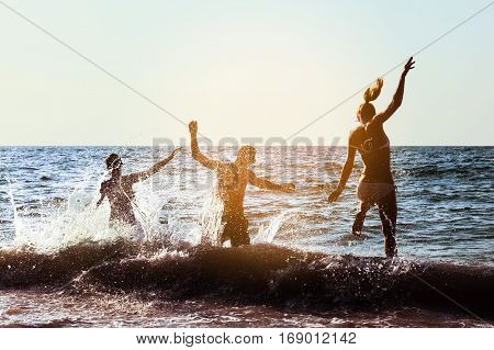 Goup of three friends having fun or dancing at beach party at sunset time. Space for text