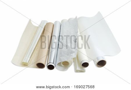 Several rolls of the plastic oven bags plastic food wrap aluminum foil and various parchment paper for household use on a light background.