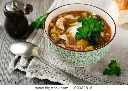 Traditional Russian soup-Rassolnik wit hpickled cucumber barley chicken tomatoes and parsley in ceramic bowl. Selective focus.