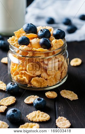 Close up of cornflackes with blackberries in jar and milk on dark wooden background selective focus vertical.