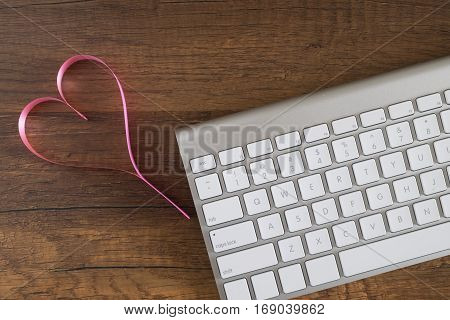 Heart Make From Pink Ribbin Near A Keyboard On Wooden Table For Anniversary; Valentine; Congratulati