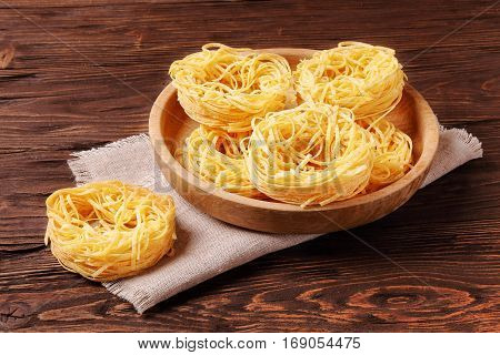 Raw pasta fettuccine in a wooden bowl on the table