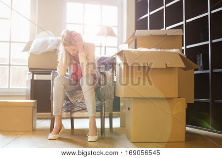 Full-length of frustrated woman sitting by cardboard boxes in new house