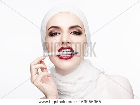 Beautiful model holding syringe in her lips for plastic surgery contept on white background
