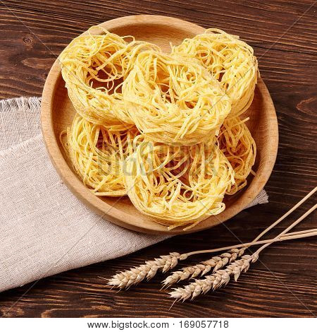 Raw pasta fettuccine in a wooden bowl on the table