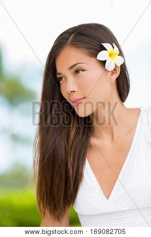 Asian mixed race beauty woman with healthy hair wearing hawaiian flower. Wellness skincare happy lifestyle. Serene multicultural girl outdoors at tropical spa. Young mixed race model on Hawaii.