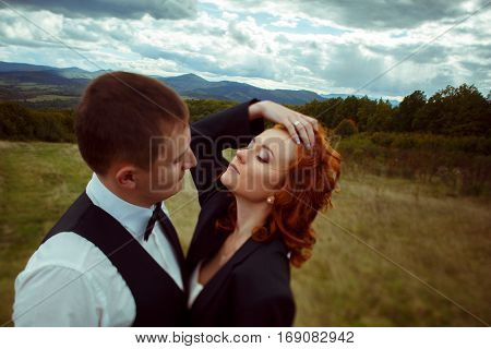 Bride Touches Her Hair Throwing Her Head Back Standing In Groom's Hugs