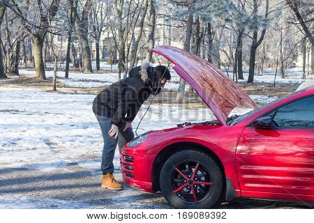 Man in trouble with his broken car .He is worried he is looking at engine under hood.