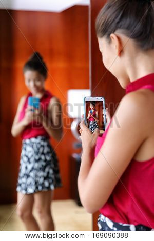 Woman taking selfies in the mirror of changing room at upscale store or at home getting ready trying on office outfit for what to wear. Weight loss, body image, self-esteem.