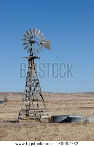 An agriculture farming windmill on the eastern plains of Colorado with the hills of the Pawnee Buttes Grasslands in the background