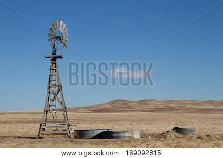 An agriculture farming windmill on the eastern plains of Colorado with the hills of the Pawnee Buttes Grasslands in the background